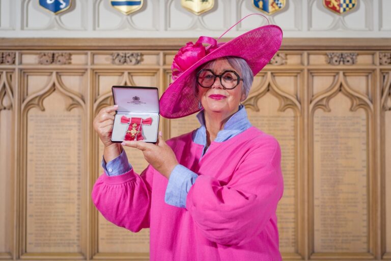 Founder and Honorary President in a large pink hat and pink outfit proudly holding her OBE.