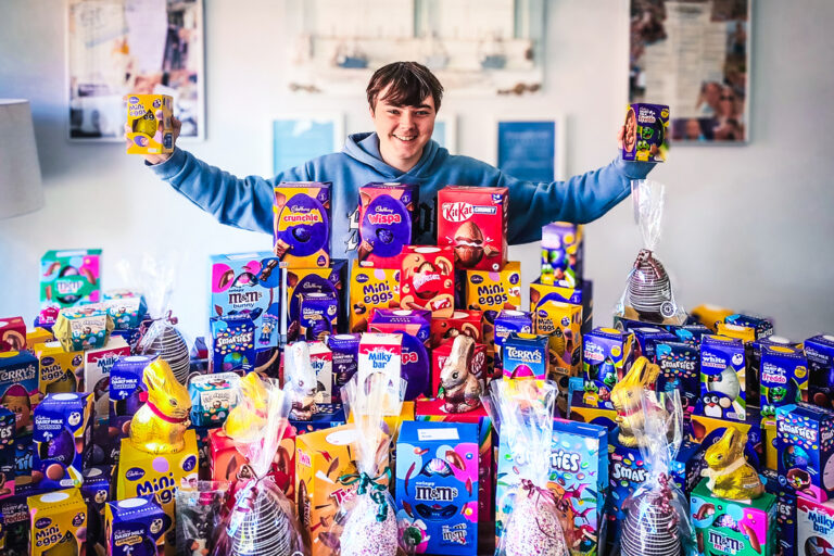 Momentum Young Ambassador standing behind his collection of Easter eggs, arms wide holding an egg in each hand.