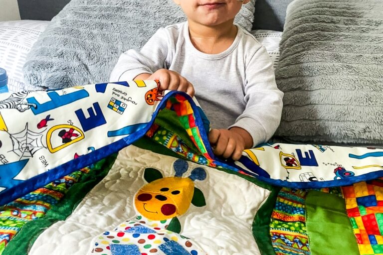 A supported child resting in a hospital bed with a nasogastric tube, covered by a quilt handmade by a Momentum volunteer.