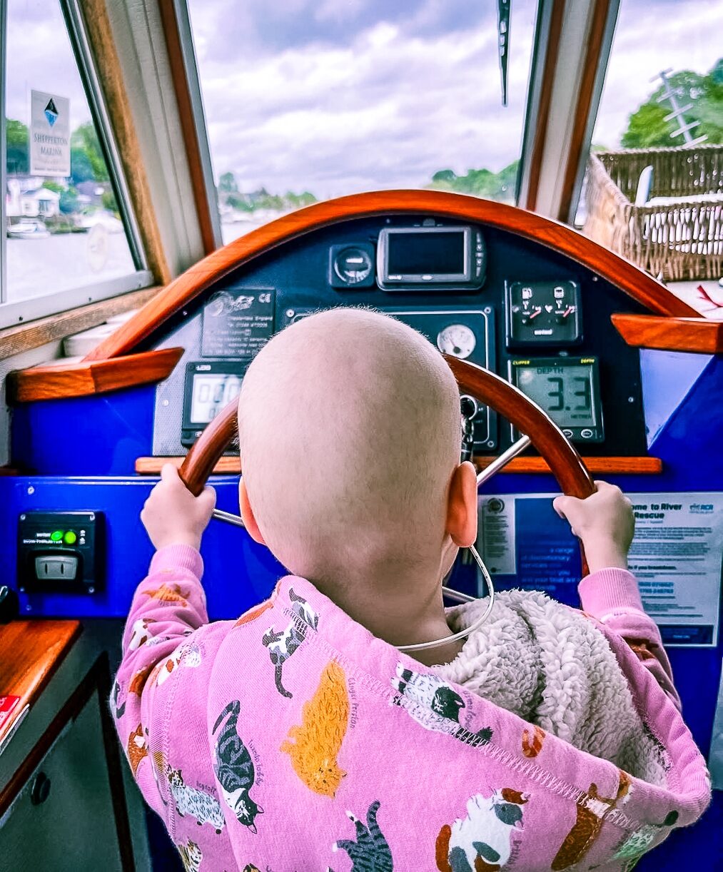 A supported child, seen from behind, driving the Momentum boat.