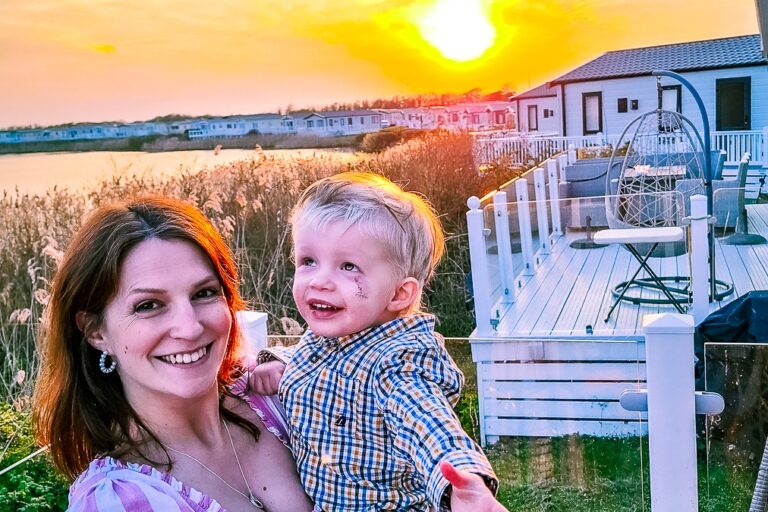 A mum and son smiling in front of the setting sun at a respite cabin.