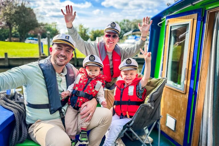 A supported family smiling and waving from the front of the Momentum boat, all wearing life jackets.