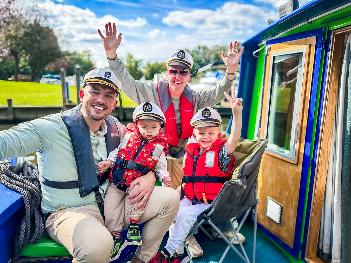 A supported family smiling and waving from the front of the Momentum boat, all wearing life jackets.
