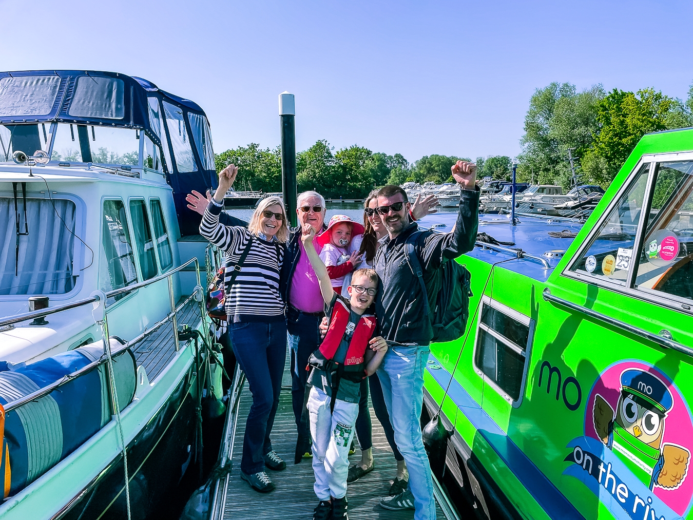 A supported family with grandparents enjoying a trip on the Momentum boat, smiling and raising their arms.