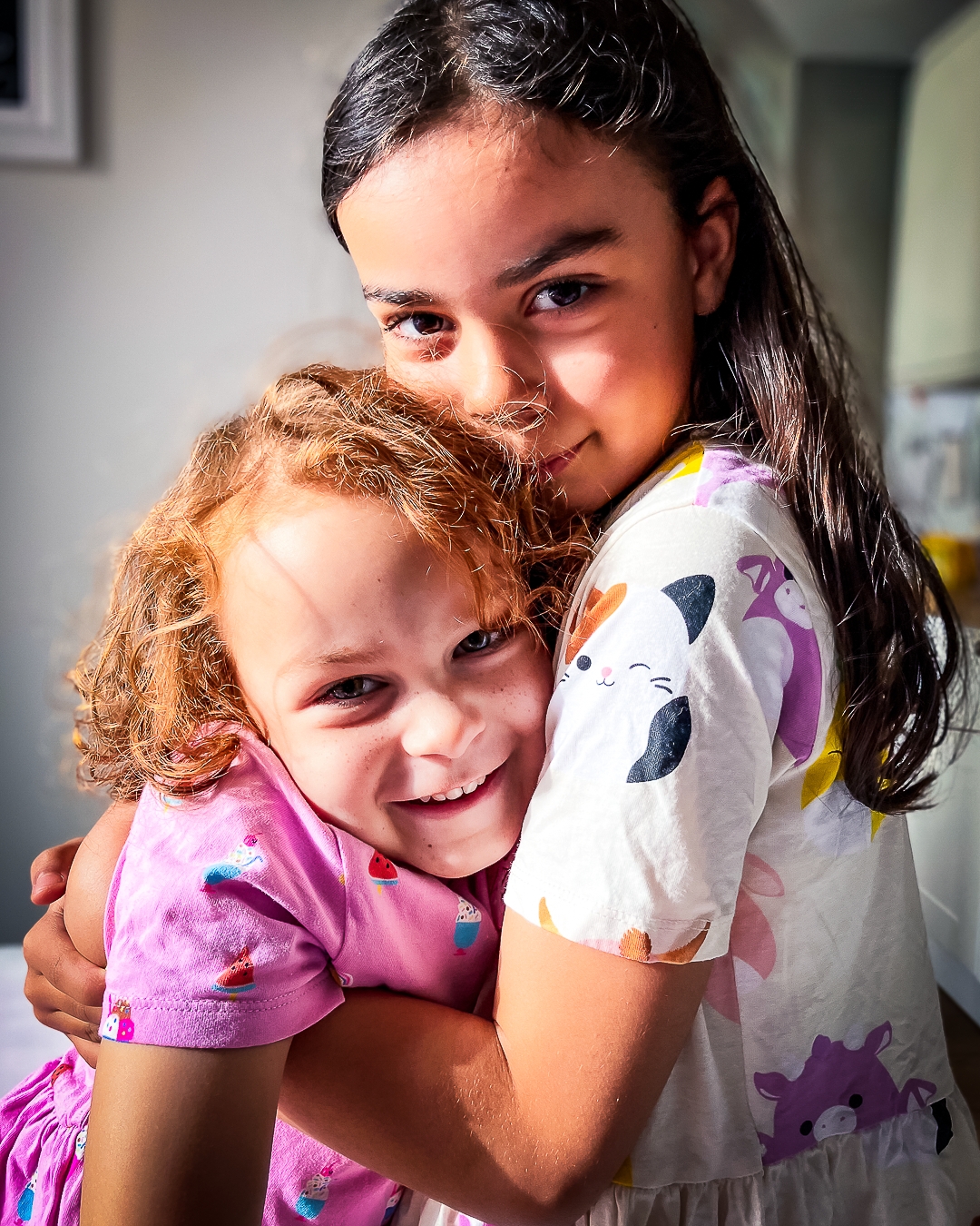 A supported child and their sister hugging and smiling at the camera.