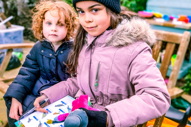 Two supported sisters reading a book together in their garden during winter.