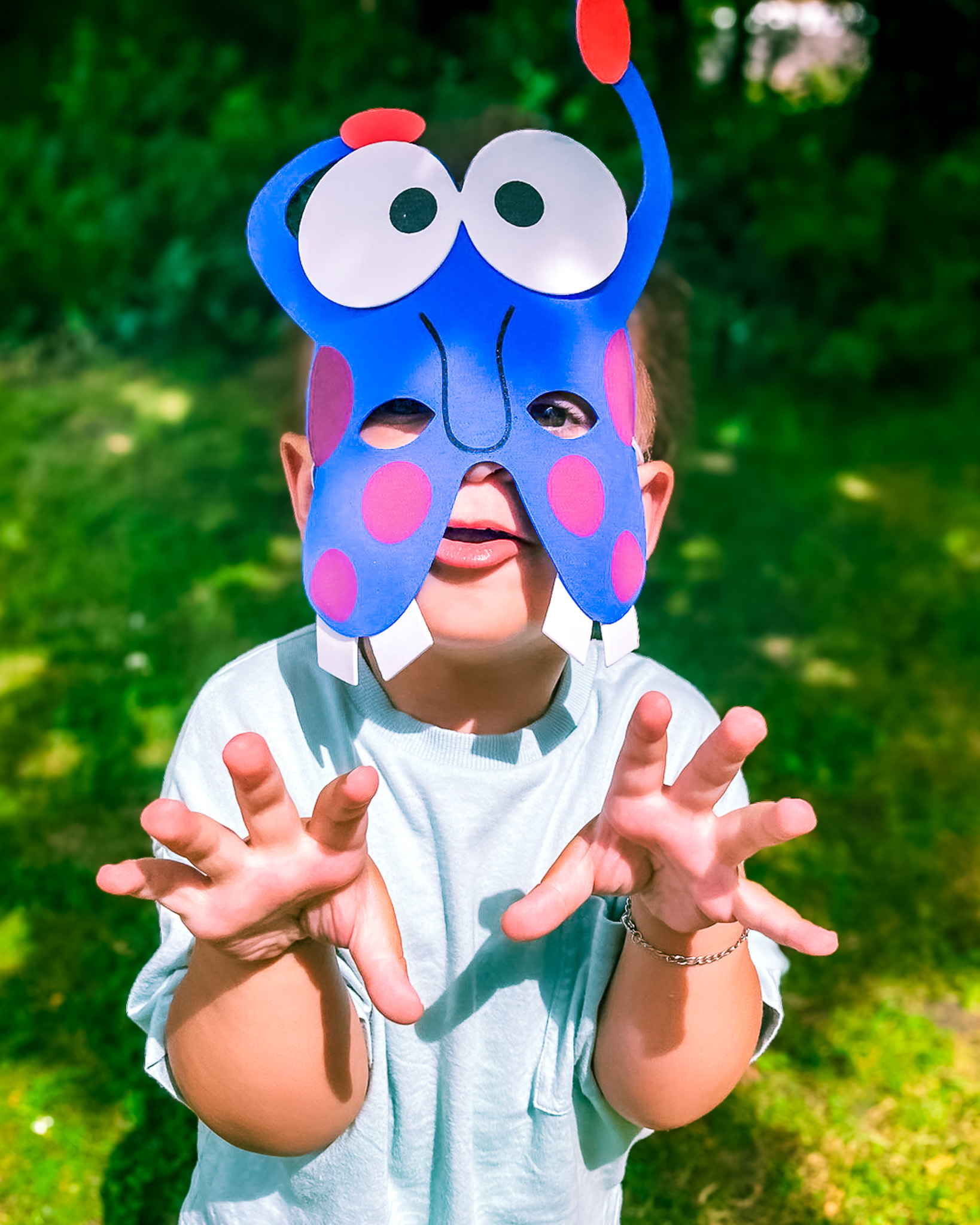 A supported child wearing a monster mask and raising his hands to the camera playfully.