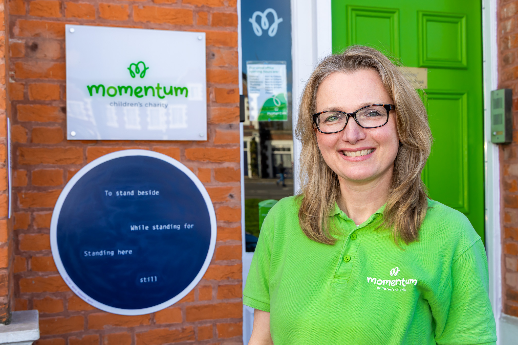 Momentum social support worker stands outside the momentum office infront of momentum logo plaque