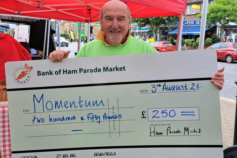 Momentum Event Volunteer poses at an event stall with a giant cheque.
