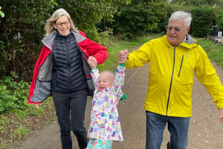 Grandparents swing their grandchild in the middle, while out walking in the countryside.