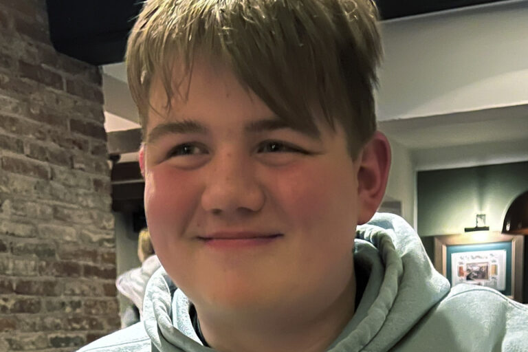 A teenage boy in a grey hoodie smiling.