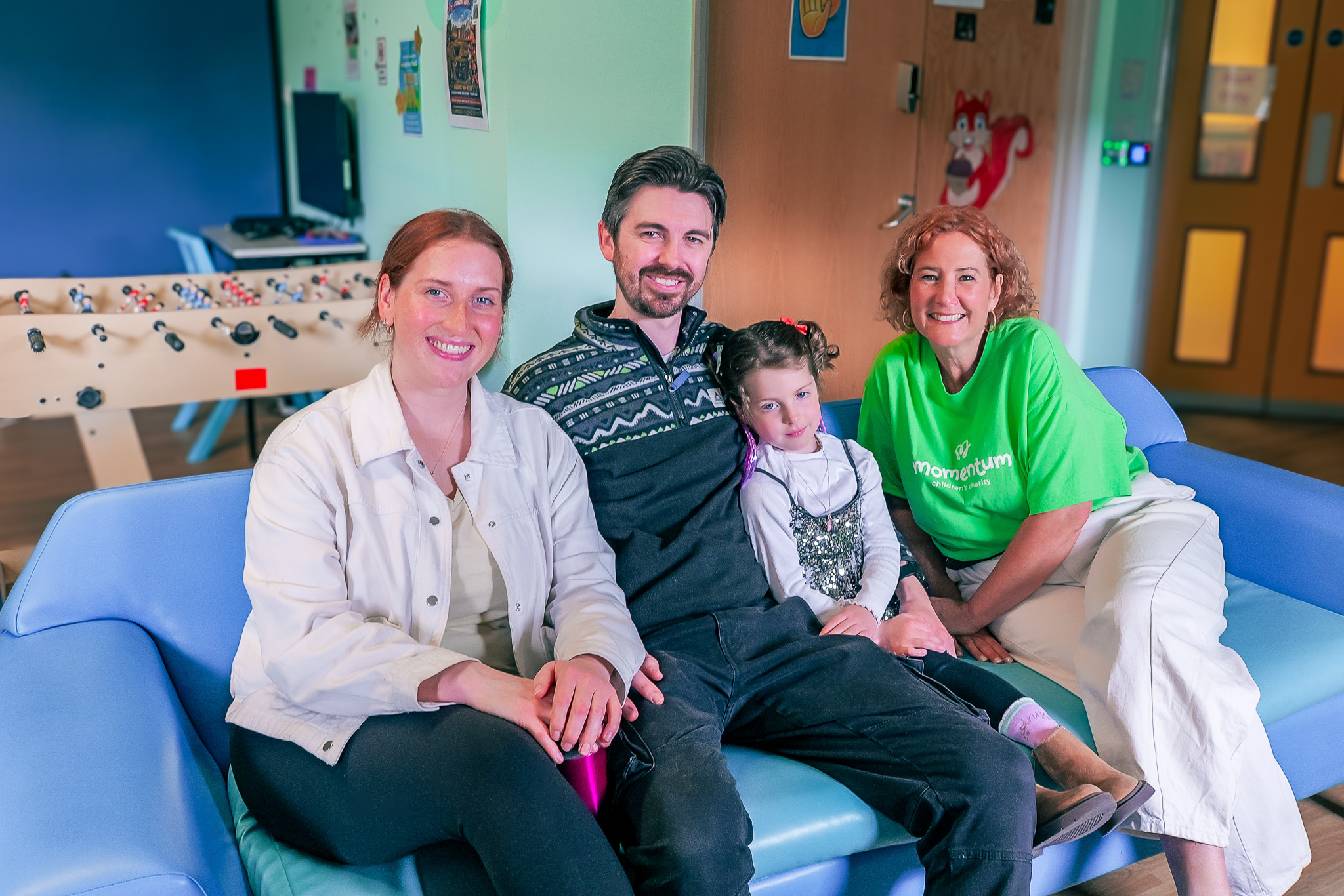A family sit on a sofa with a Momentum Children's Charity staff member