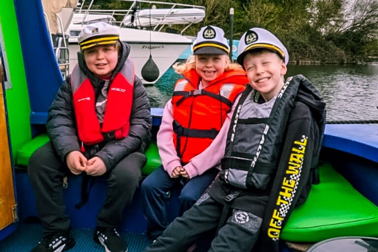 Three children sit aboard Momentum Children's Charity's riverboat on The Thames.