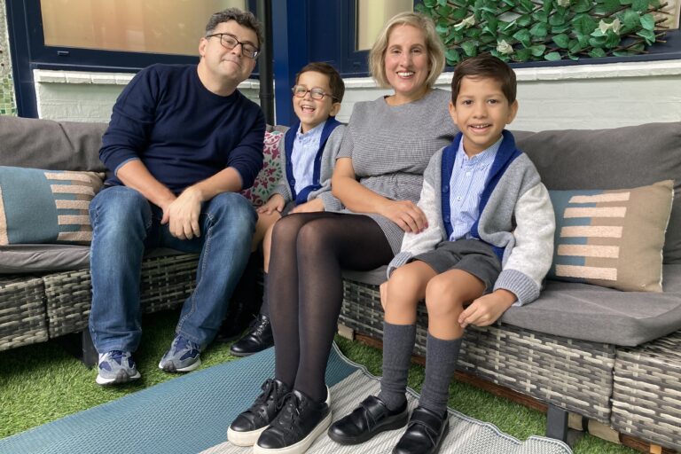 A family supported by Momentum sits on a sofa together. The two young boys are in school uniform.