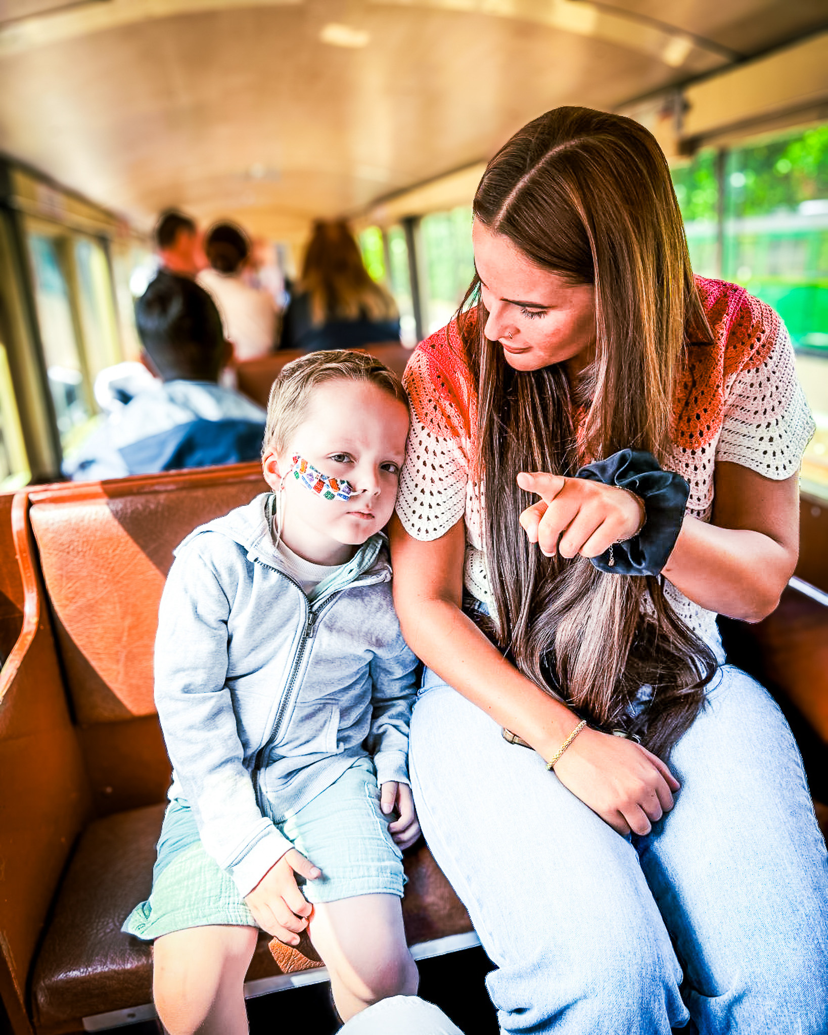 A young boy with a nasal tube taped to his cheek rests against his mum's shoulder on a steam train, sharing a quiet, comforting moment.
