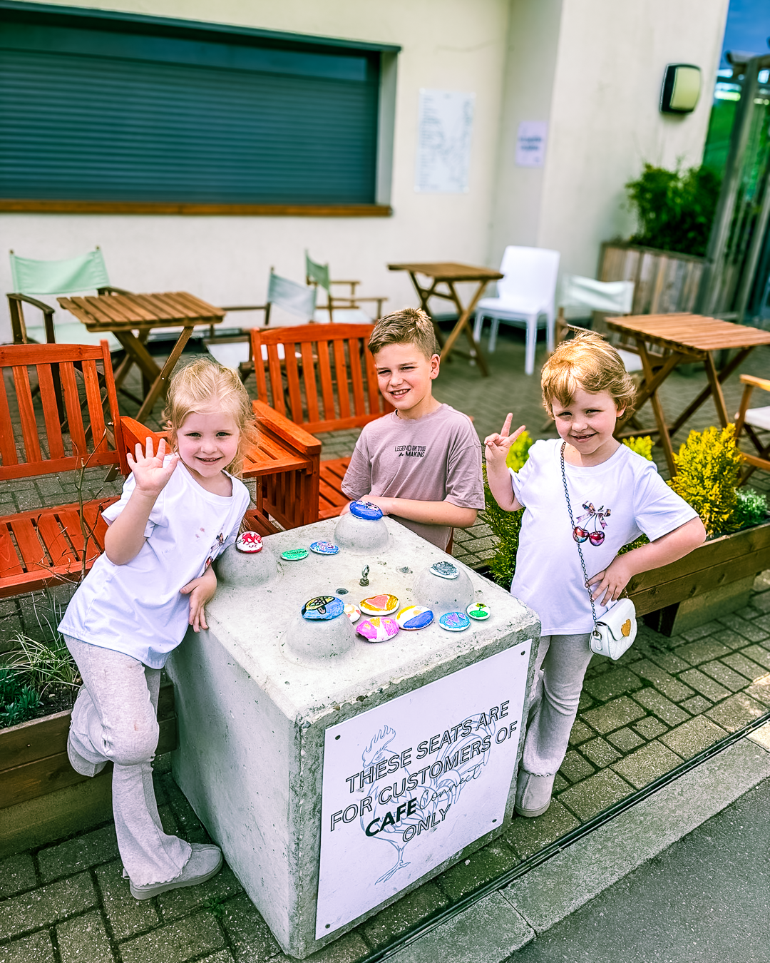 Three children - two girls and a boy smile as they paint pebbles at a Momentum event.