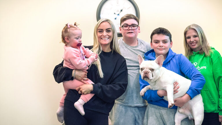 Momentum supported family standing with their family support worker in front of a clock in their home