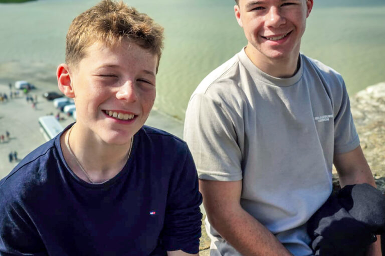Two teenage brothers sitting next to each other smiling on holiday.