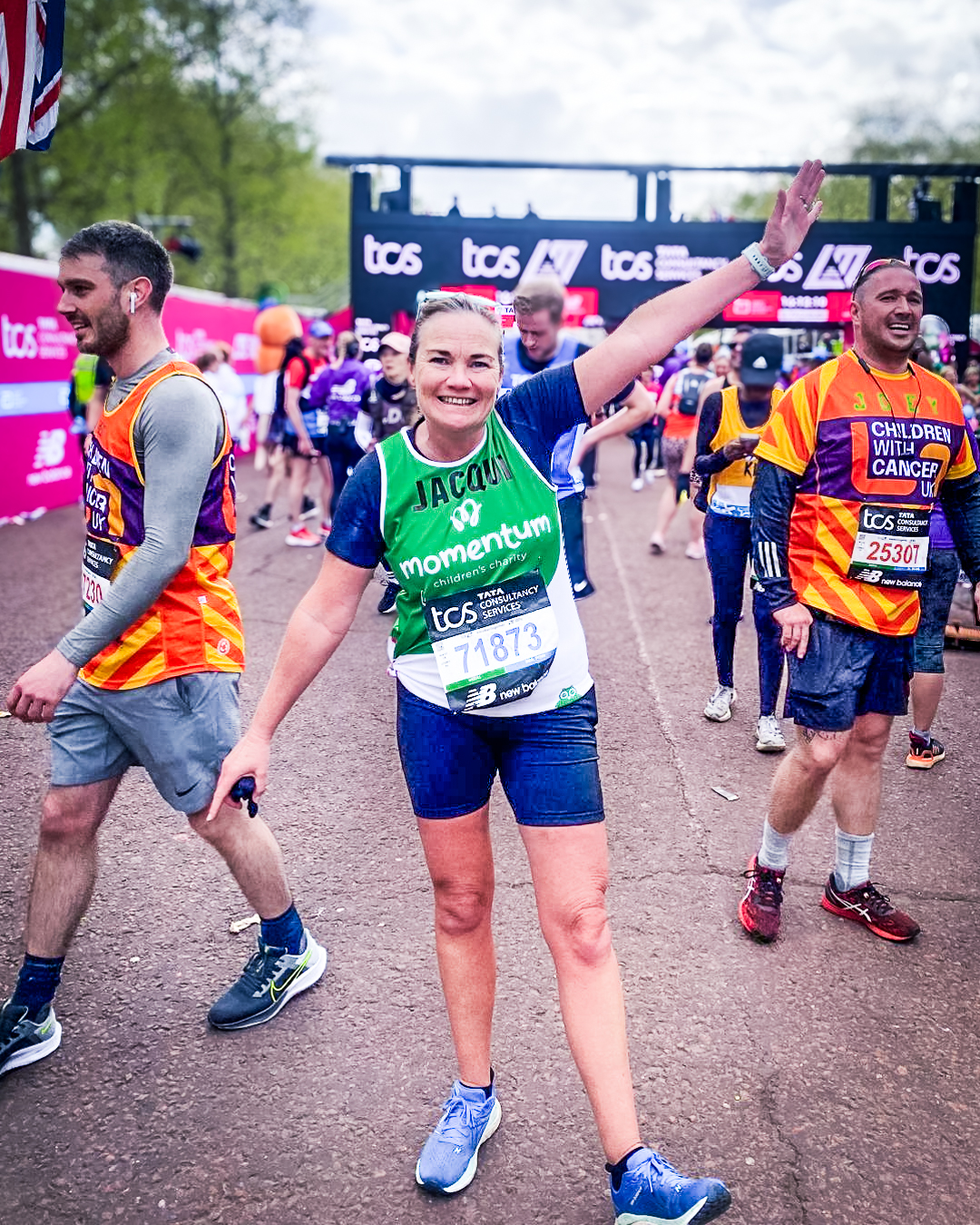 A runner in the TCS London Marathon celebrates with arms out after completing the marathon for Momentum in her green Momentum branded running vest.