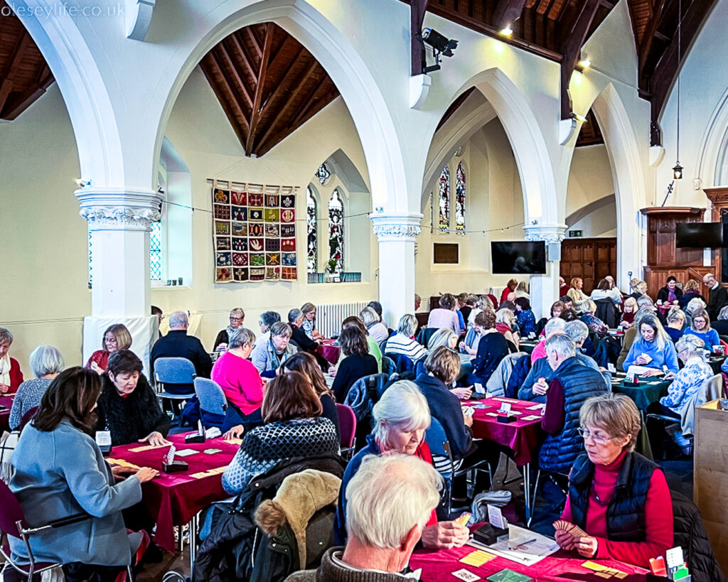 A group of people gathered in a church location playing a bridge tournament to help raise money for charity