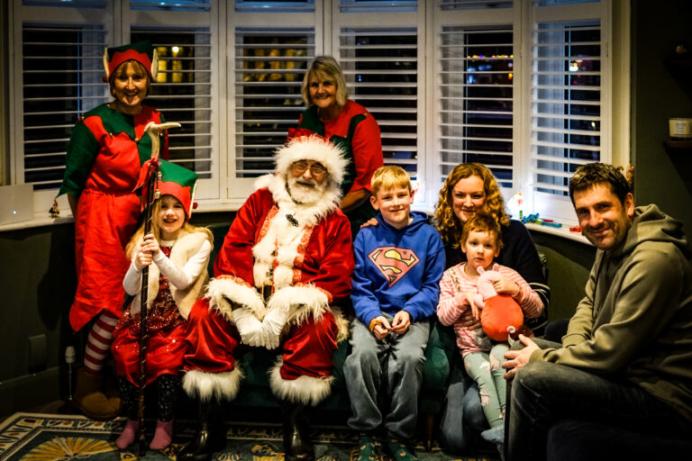 A Momentum-supported family with three children receive a visit from Santa and his two helpers. They sit together in the lounge.