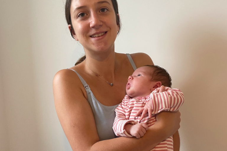 A young woman, once supported by Momentum, smiles for the camera holding her new baby.