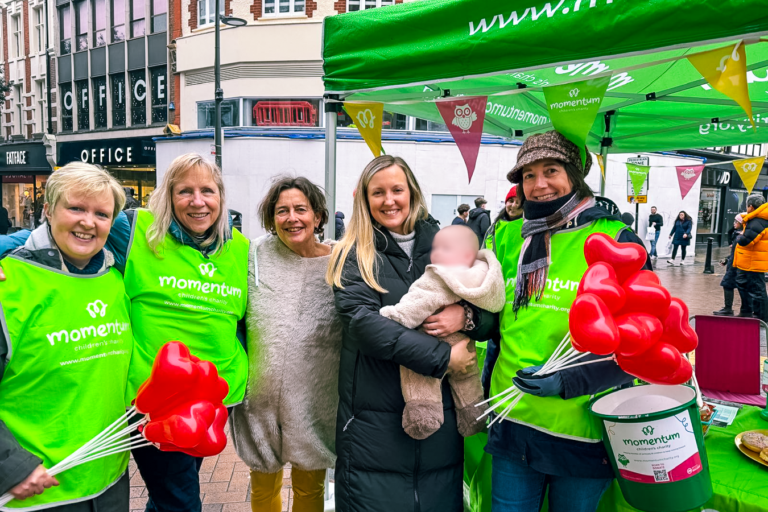 Four Momentum volunteers pose at a Valentine's Day fundraiser in Kingston, along with a mum and her baby.