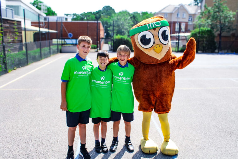 Three school children in Momentum t-shirts stand in the playground around Mo the Owl