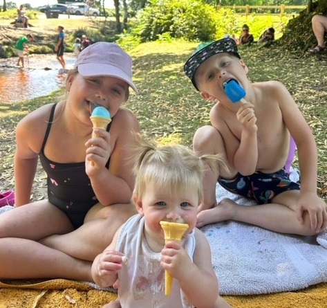 Three children in summer wear and hats licking ice creams.