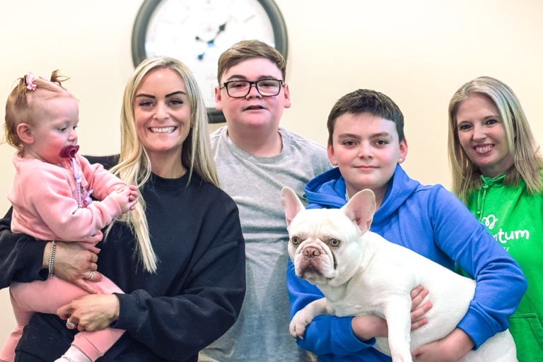 A smiling family of four together with their Family Support Worker. One of the boys is holding a dog and mum has a toddler in her arms.