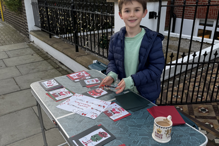 Young boy sells Christmas cards he has made to raise funds for Momentum on a table in the street.