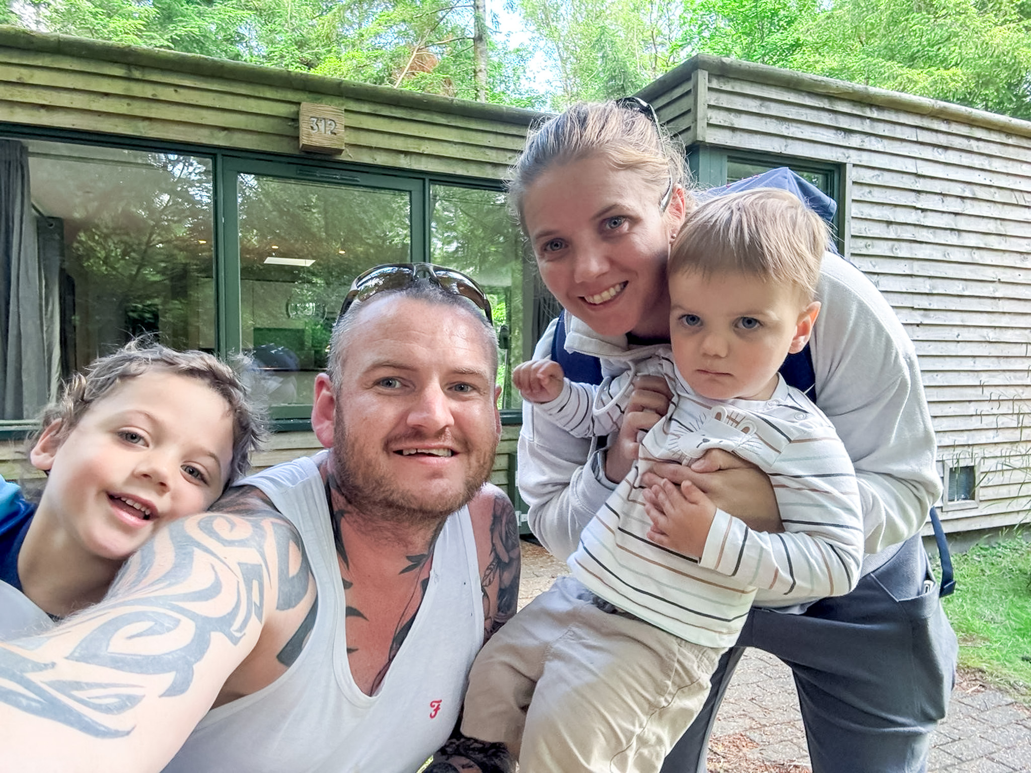 A supported family take a selfie outside a holiday cabin in the woods.