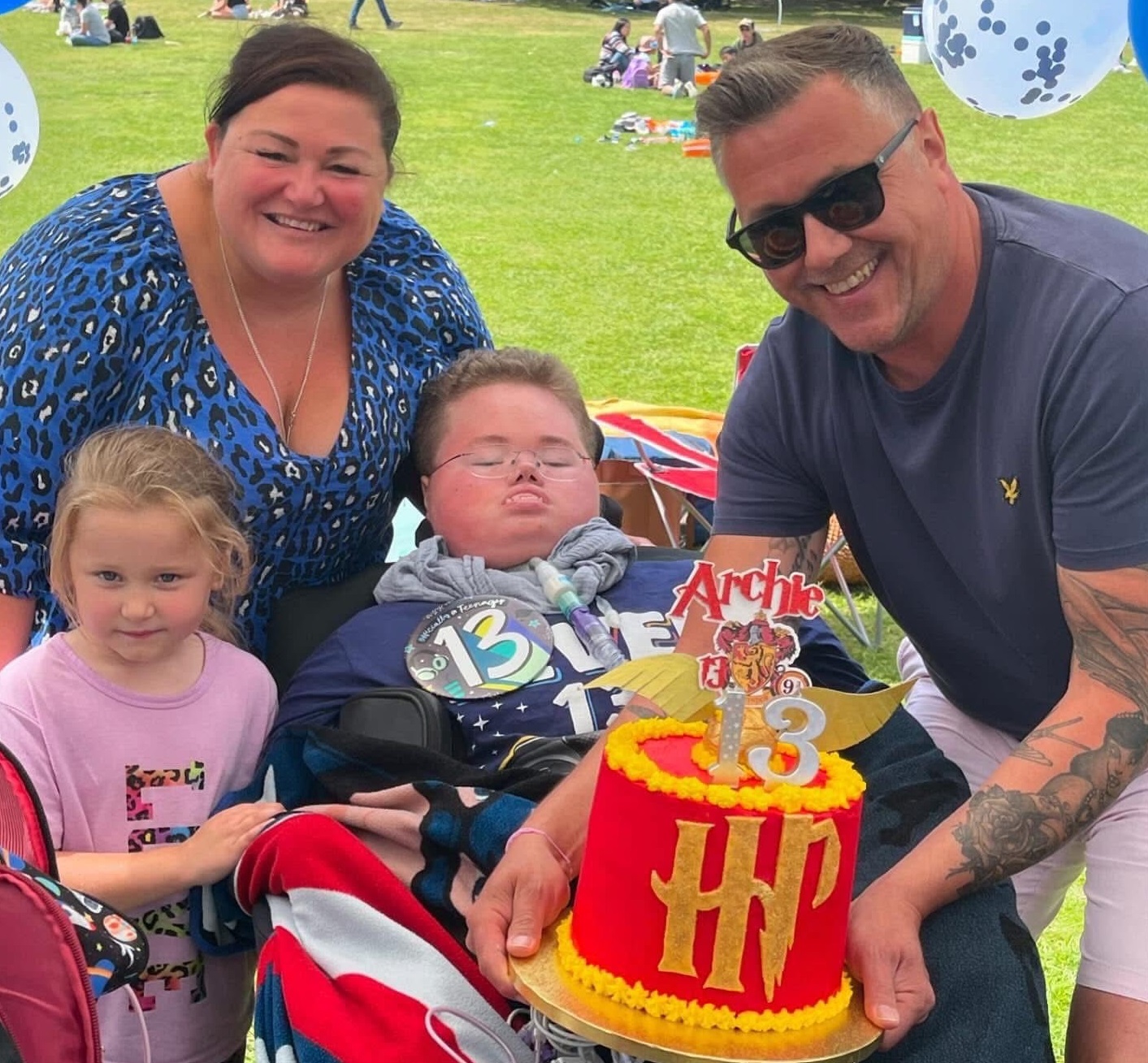 A supported family cluster around boy in a wheelchair and show off his Harry Potter-themed 13th birthday cake.