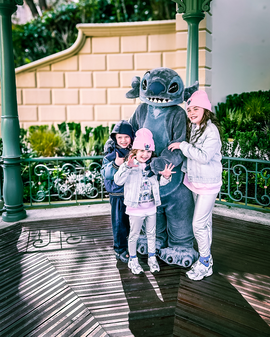 Three children cluster around a 'Stitch' mascot at a theme park.