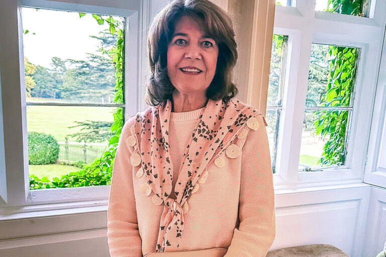 A woman smiles in front of a window.