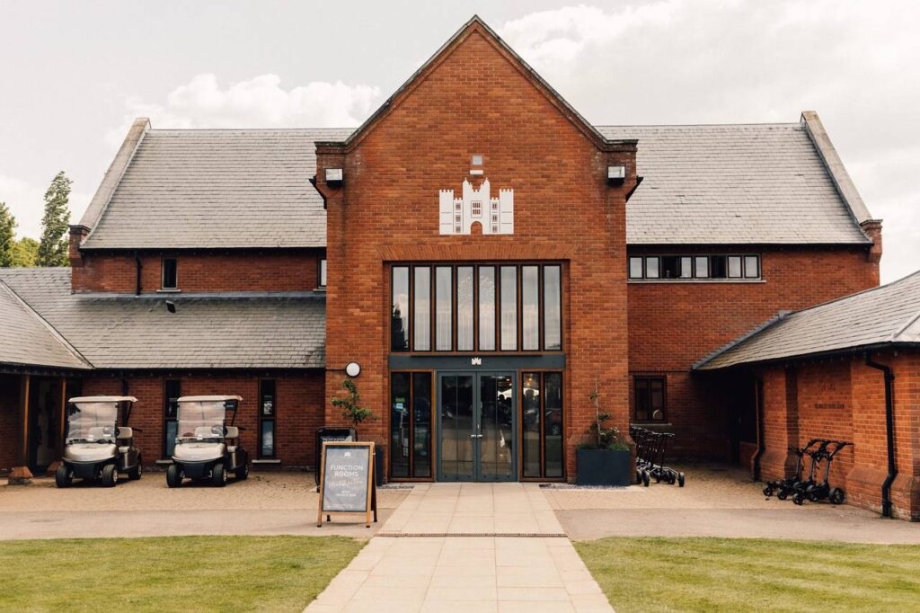 A large red bricked building with glass doors and a paved walkway leading up to them. There are golf buggies parked outside.