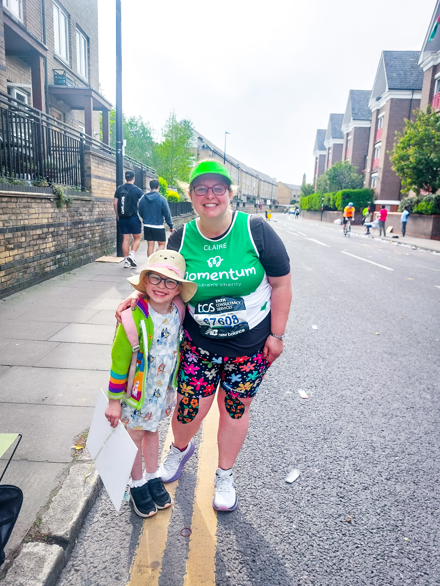 A supported child and her mum smile at the camera during the TCS London Marathon. Mum wears a Momentum T-shirt.