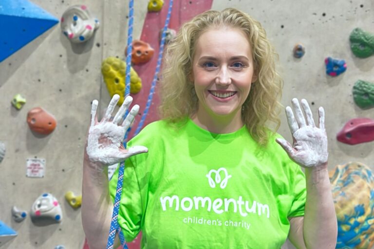 A Move for Momentum fundraiser prepares for her wall climbing challenge with chalked hands standing by the climbing wall