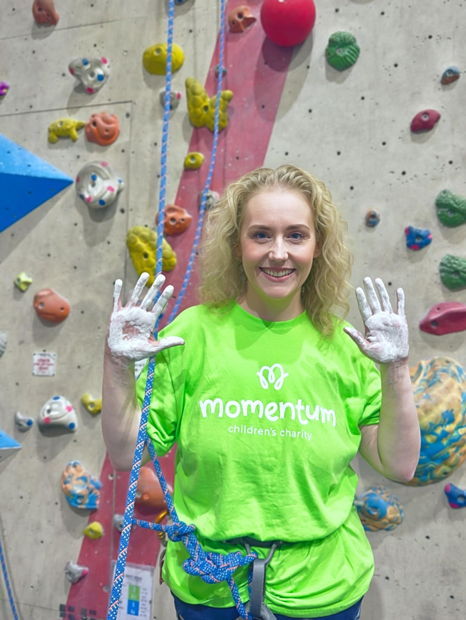 A Move for Momentum fundraiser prepares for her wall climbing challenge with chalked hands standing by the climbing wall