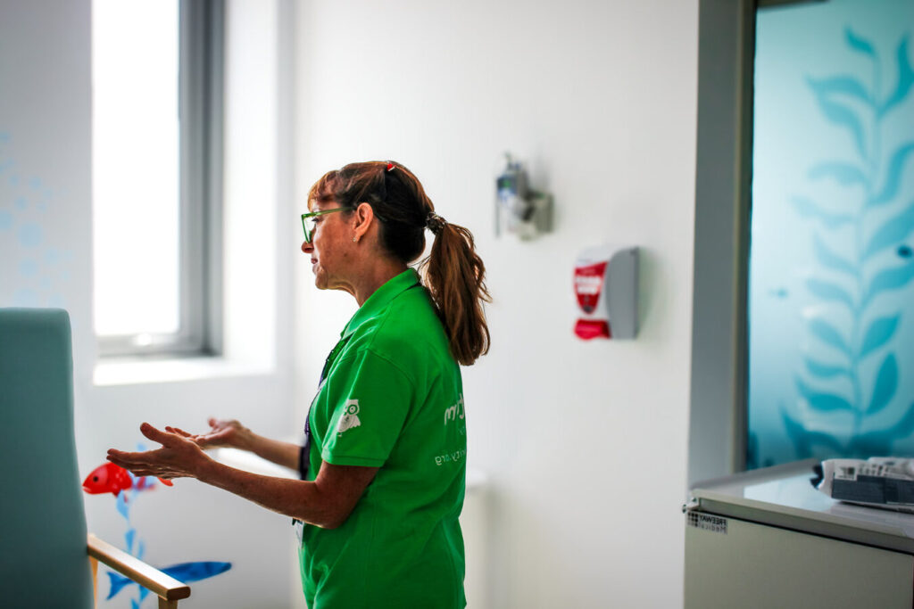 Side profile of a Momentum Children's Charity family support worker in a green Momentum polo seen at the hospital speaking with a family off-camera.