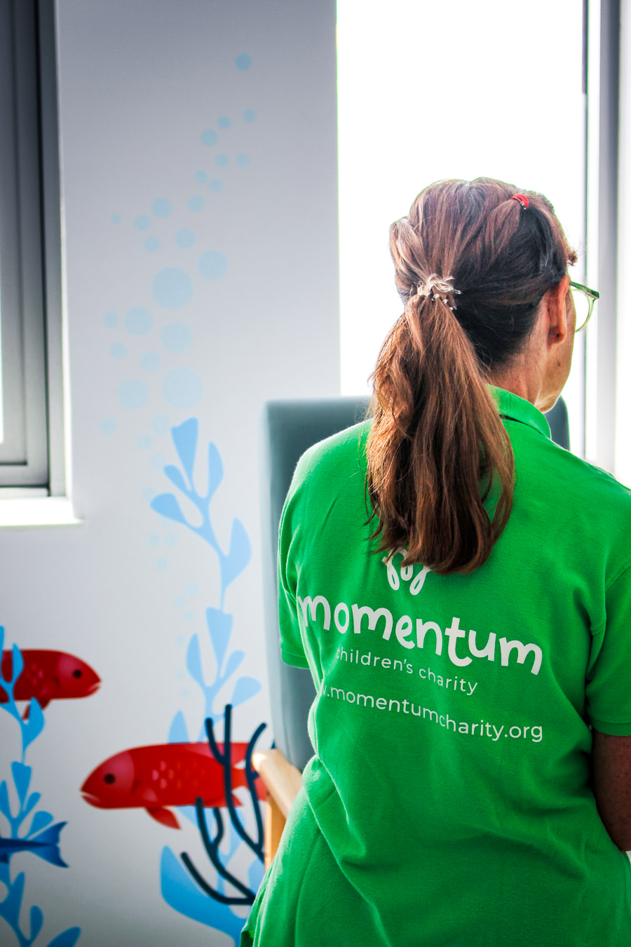 A Momentum Children's Charity family support worker in a green Momentum polo seen at the hospital speaking with a family off-camera.