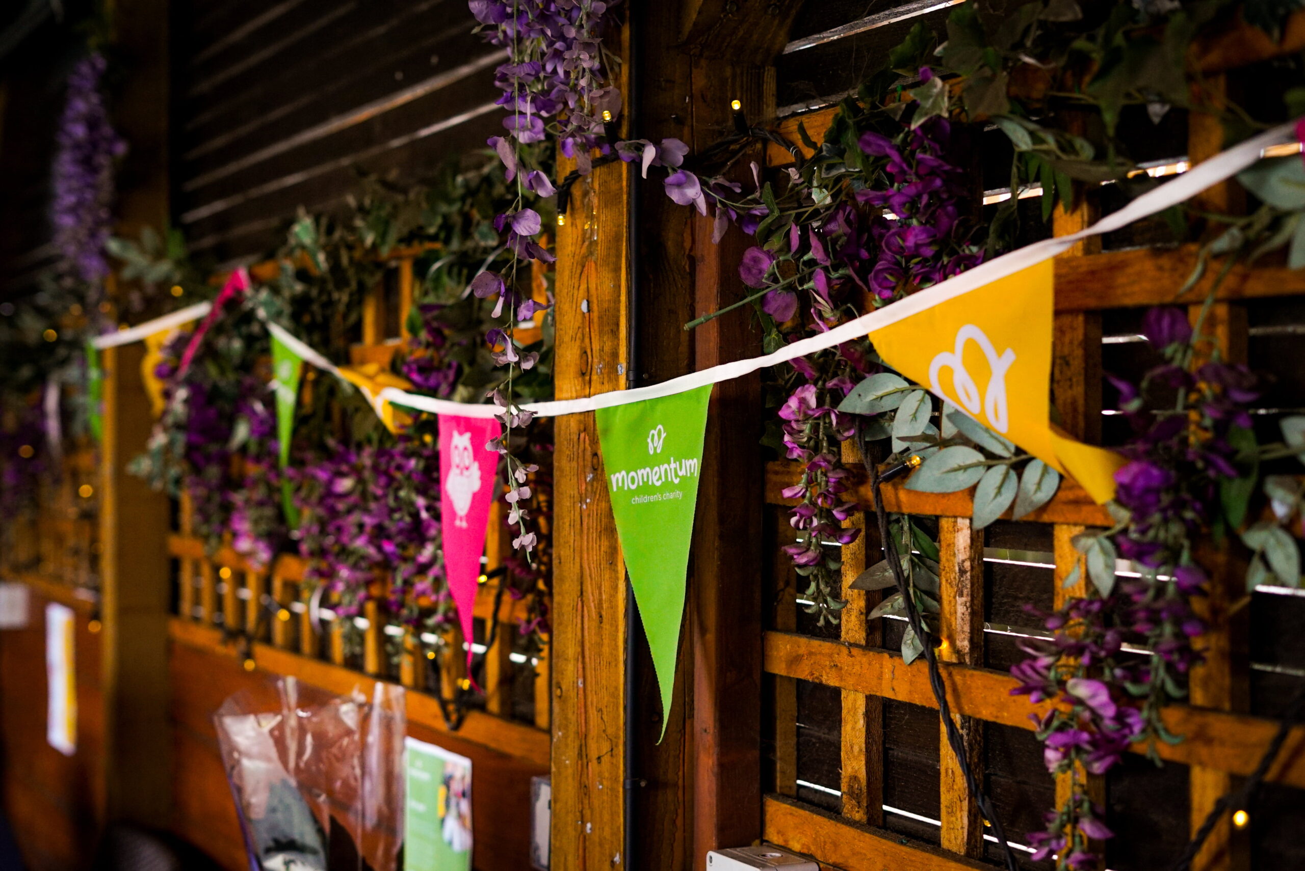 A string of Momentum branded bunting hanging up on a trellis covered in flowers.