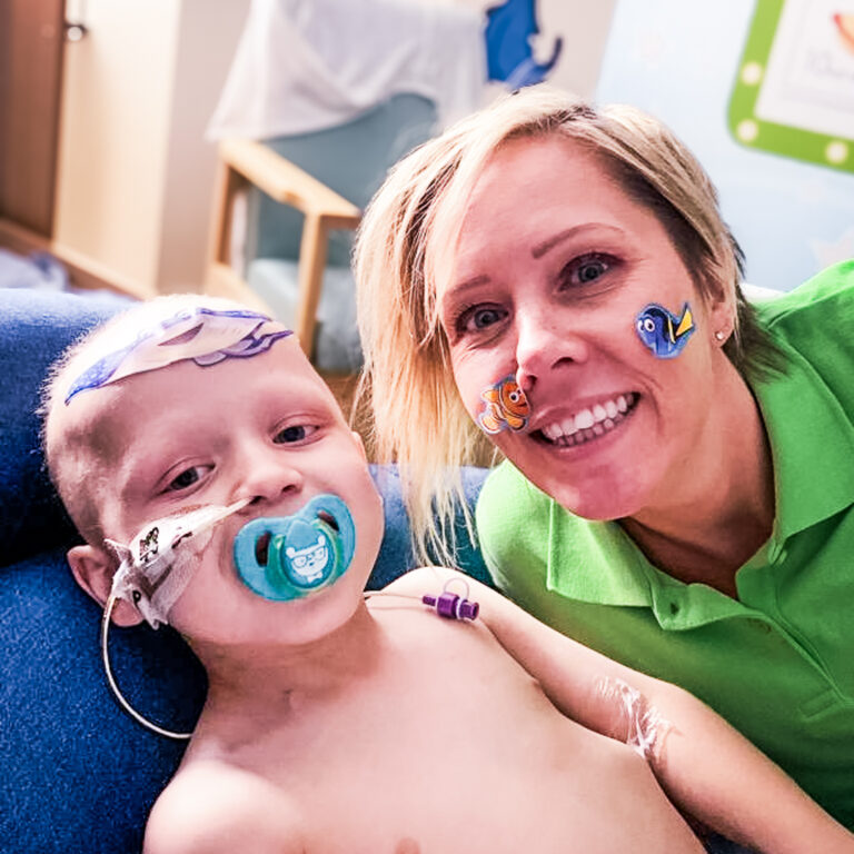 A Momentum Family Support worker leans in beside a child undergoing treatment on a hospital bed.