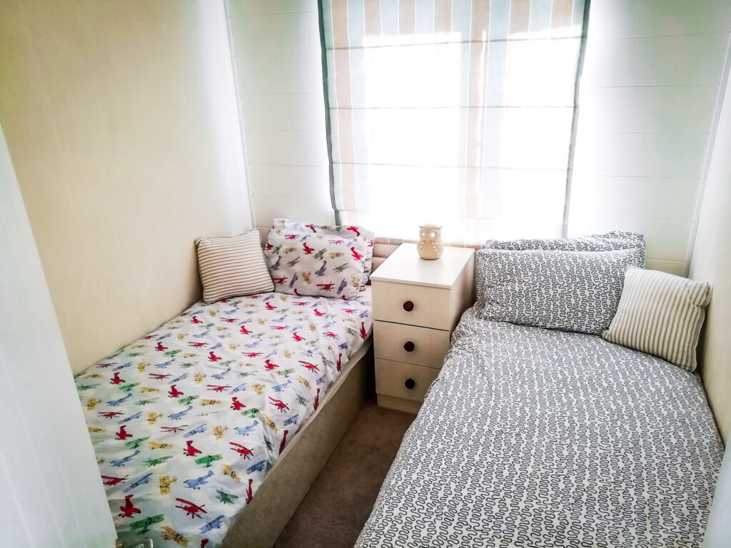 A twin bedroom at Momentum's respite cabin at Shorefield Holiday park. The bedding is patterned with aeroplanes and wiggles, and an owl night light sits on the bedside table.