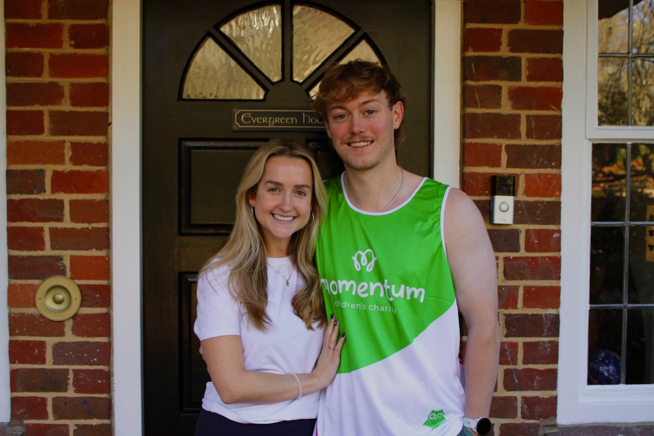 A girl stands outside a green door with her boyfriend who wears a green Momentum running top.