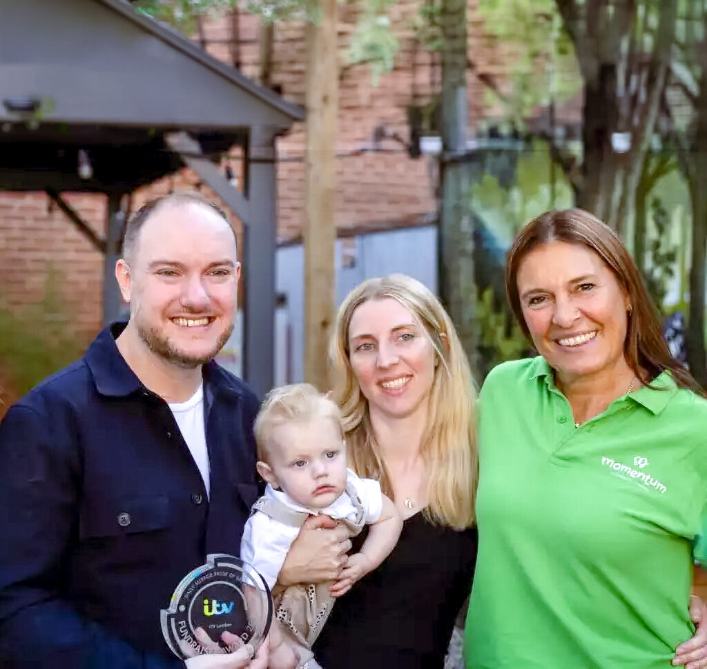 Echoes support Manager, Vanessa, and a Echoes family at a local surrey event. The smile at the camera. Vanessa is wearing a Momentum green Tshirt. There is a family beside her sniling of a mother, father and small child in the Mother's arms.