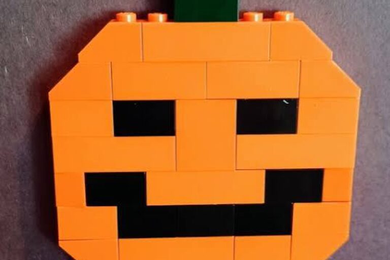 An orange pumpkin with a carved out smiling face made out of Lego bricks.