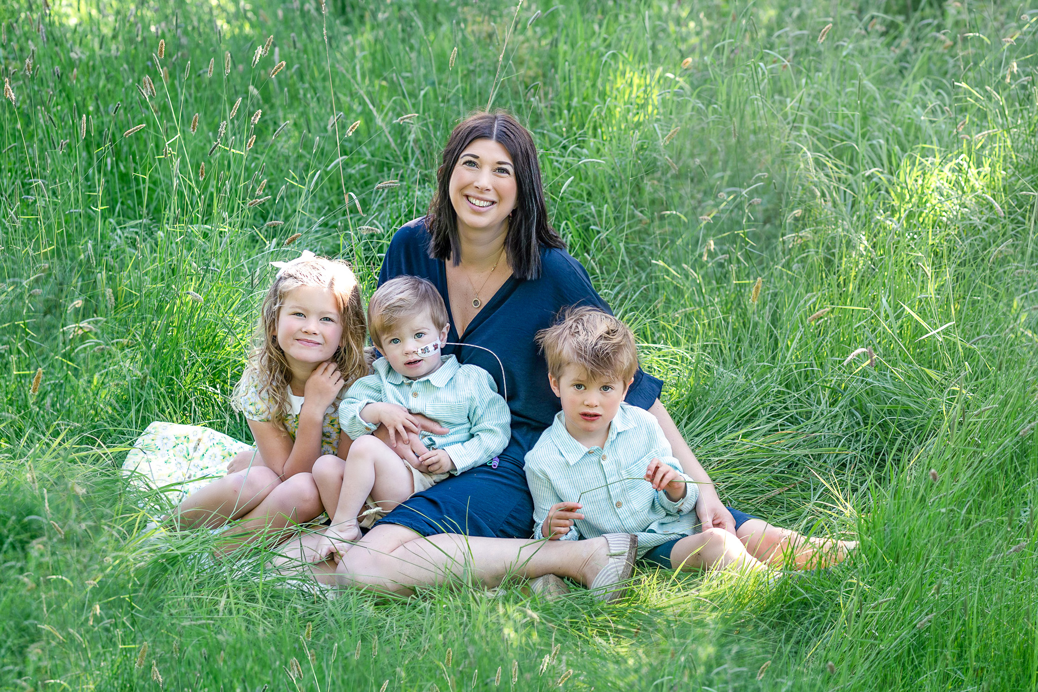 Supported family - a mother and her three children sit in a lush green field in summer clothing.
