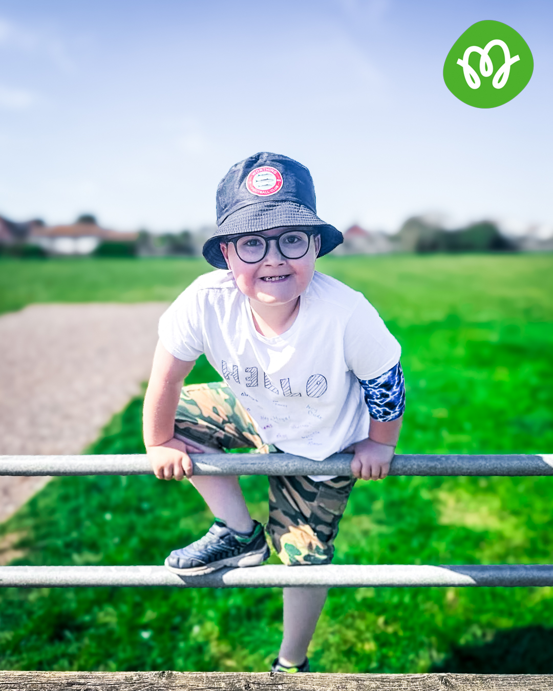 Small boy smiling as he climbs over a fence in the countryside