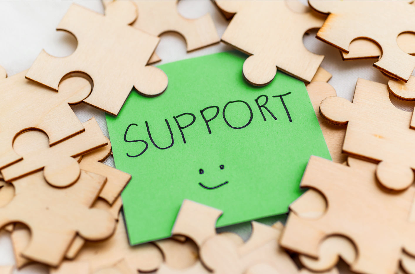 Wooden puzzle pieces arranged around a green post-it papaer with the word "Support" written by hand and smiley face.